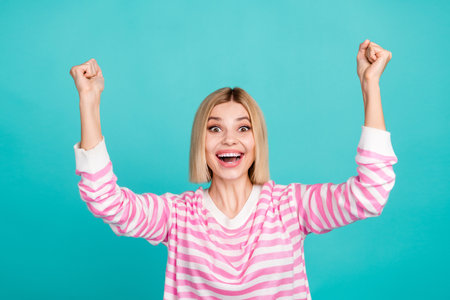 Photo of shocked impressed girl dressed striped sweater shouting yeas rising fists isolated teal color backgroundの写真素材