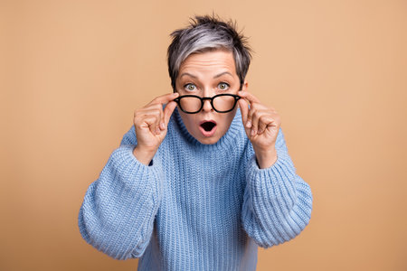 Portrait of impressed speechless lady arms touch glasses open mouth staring isolated on beige color backgroundの写真素材