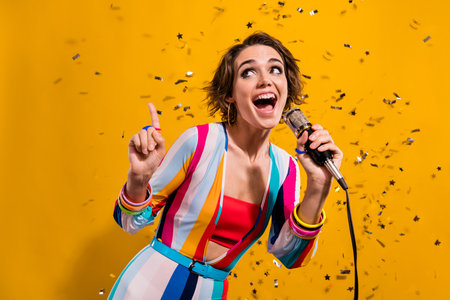 Photo of having fun girl finger up novelty singer solo vocalist retro clothes bright outfit cable mic isolated on yellow color backgroundの写真素材