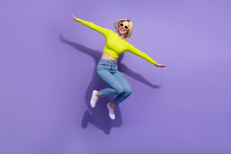 Full length photo of cheerful glad girl wear trendy clothes have fun fly air empty space isolated on purple color backgroundの写真素材