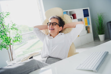 Photo of beautiful manager worker elderly woman hands head satisfied leather chair workshop time out pause isolated on office backgroundの写真素材