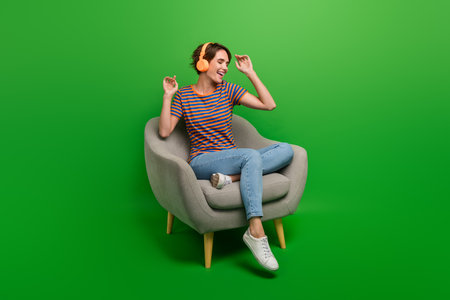 Full size photo of excited positive girl sit cozy soft chair enjoy listen favorite song isolated on green color backgroundの写真素材