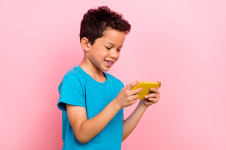 Photo portrait of pretty schoolboy hold device watch video play mobile game dressed stylish blue outfit isolated on pink color backgroundの写真素材