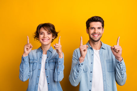 Photo of satisfied optimistic wife husband friends denim trendy outfit arms demonstrate empty space isolated on yellow color backgroundの写真素材