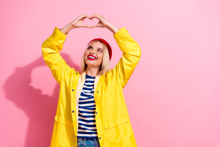 Portrait of sweet hipster girl enjoy garment fingers show heart symbol looking dreamy new waterproof coat isolated on pink color backgroundの写真素材