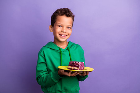 Photo of pretty funky little boy dressed green hoodie holding cake piece plate empty space isolated purple color backgroundの写真素材