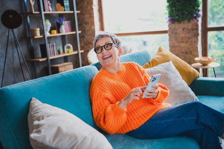 Photo of cheerful pretty lady sit comfy couch use smart phone brainstorming enjoy spend pastime flat...