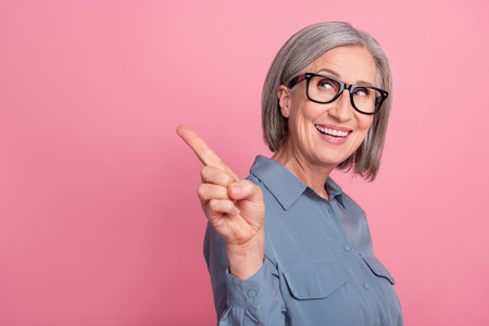 Photo of attractive positive pensioner wear trendy clothes presenting empty space stomatology veneers isolated on pink color backgroundの写真素材