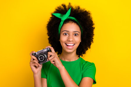 Portrait of positive lovely person toothy smile have good mood hands hold photo camera isolated on yellow color backgroundの写真素材