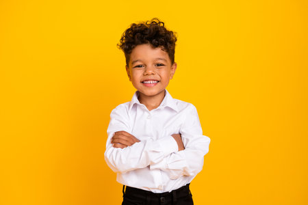 Portrait of adorable cheerful schoolboy with wavy hair wear stylish shirt standing hold arms crossed...