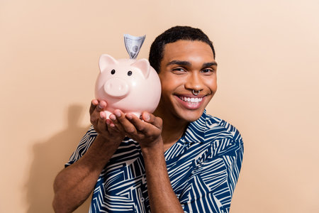Photo portrait of handsome young guy hold money pig dollar insert wear trendy blue print outfit isolated on beige color backgroundの写真素材