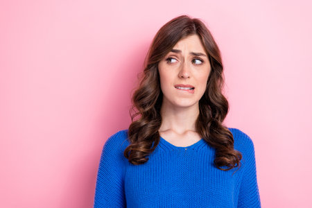 Photo of anxious embarrassed girl dressed blue pullover bite lips looking empty space isolated on pink color backgroundの写真素材