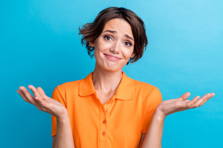 Photo of doubtful unsure girl dressed orange polo shrugging shoulders isolated blue color backgroundの写真素材