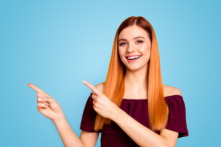 Close up portrait of cheerfully laughing young woman showing by her fingers on yellow background with copy space for textの写真素材
