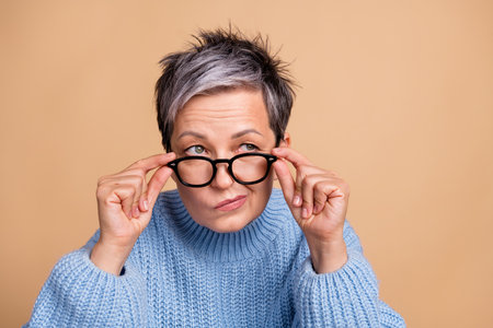 Photo of minded intelligent person hands touch eyeglasses look empty space isolated on beige color backgroundの写真素材