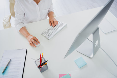 Cropped photo of mature lady worker wear white shirt communicating modern device indoors workplace workstationの写真素材