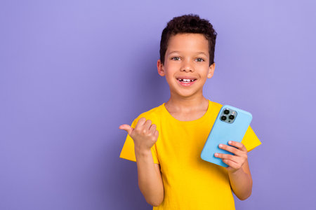 Photo of beautiful satisfied boy wear yellow trendy clothes arm demonstrate empty space promo banner isolated on purple color backgroundの写真素材