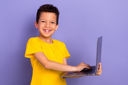 Photo of positive nice boy wear yellow trendy clothes use modern netbook device isolated on purple color backgroundの写真素材