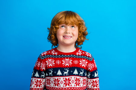 Photo of positive thoughtful little boy dressed ugly pullover looking up empty space celebrating...