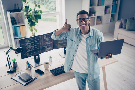 Photo of junior it specialist young guy web products developer holding laptop thumb up gesture enjoy his programming job in officeの写真素材