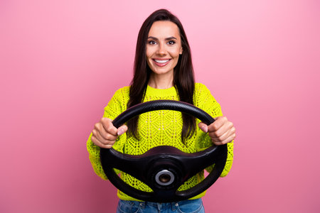 Photo of adorable pleasant girl with brunette hair dressed yellow sweater holding streering wheel isolated on pink color backgroundの写真素材