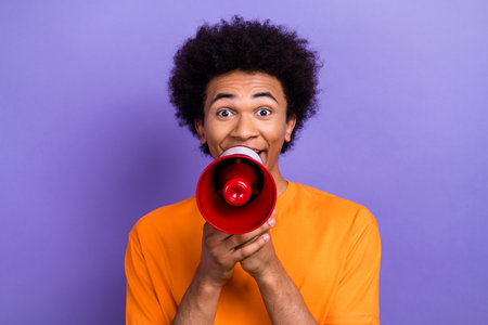 Photo portrait of screaming young guy holding megaphone support his demonstration human rights isolated on purple color backgroundの写真素材