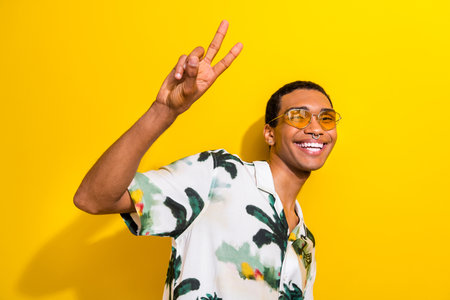 Photo of attractive positive nice guy wear trendy clothes sunglass hand demonstrate v-sign isolated...