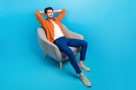 Full body photo of calm carefree nice person sit cozy chair closed eyes arms behind head isolated on blue color backgroundの写真素材