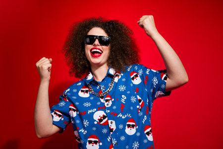 Photo of funky lucky woman wear ugly santa claus print x-mas shirt screaming rising fists isolated...