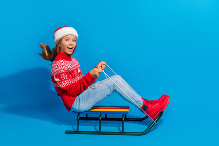 Full length photo of overjoyed excited teen girl wear jumper santa hat goes on sleigh to empty space...