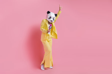 Full length of cool carefree person 3d panda mask point finger sing microphone empty space isolated on pink color backgroundの写真素材