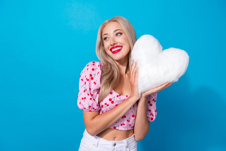 Photo portrait of lovely young lady hold plush white heart pillow wear trendy pink cherry print garment isolated on blue color backgroundの写真素材