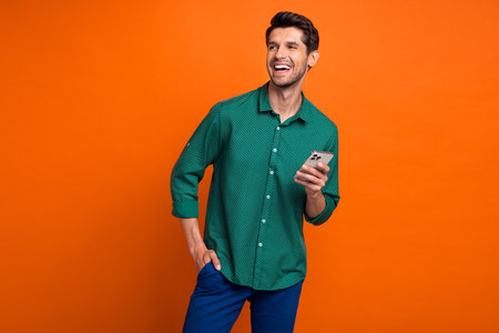 Photo of young laughing guy browsing phone repost new content smm manager laugh look novelty isolated on orange color backgroundの写真素材