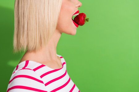 Profile photo of young girl holding open mouth teeth red fresh healthy strawberry summer agriculture isolated on green color backgroundの写真素材