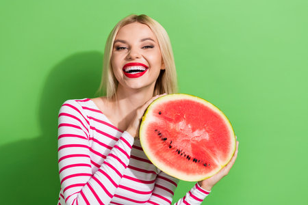 Photo of young girl wear striped trendy top hold fresh juicy watermelon eating summer seasonal berry isolated on green color backgroundの写真素材