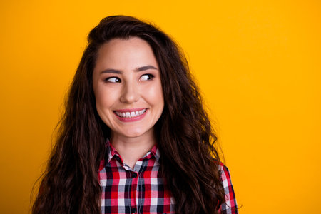 Portrait of satisfied optimistic person with curly hairstyle wear plaid shirt look at sale empty space isolated on yellow backgroundの写真素材