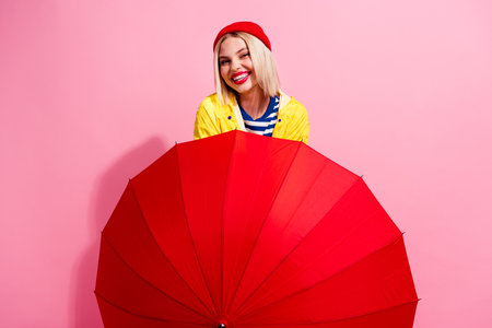 Photo of excited adorable lady wear raincoat walking under umbrella isolated pink color backgroundの写真素材