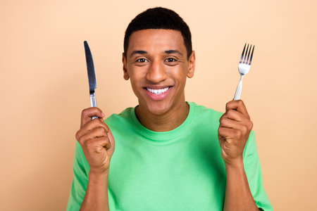 Photo portrait of handsome young male hold fork knife eating food wear trendy green outfit isolated on beige color backgroundの写真素材