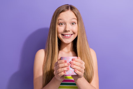 Portrait of optimistic impressed teen girl with long hairstyle wear colorful singlet holding cup of tea isolated on purple backgroundの写真素材