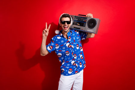 Photo of friendly guy showing v sign clubber holding old school boombox for christmas eve...