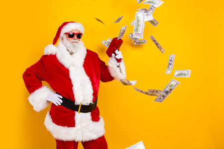 Photo of cool funny santa claus old man shooting flying banknotes money gun casino winner jackpot isolated on yellow color backgroundの写真素材