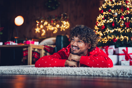 Photo of dreaming young funny arabian guy folded arms lying floor carpet looking curious wish about big family in next 2024 new yearの写真素材