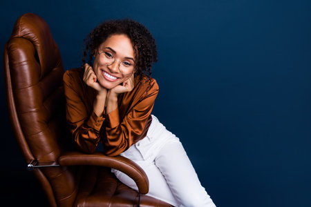 Photo portrait of attractive young woman ergonomic chair cute dressed stylish brown silk formalwear isolated on dark blue color backgroundの写真素材
