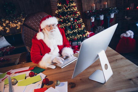 Photo of good mood funky santa claus dressed red costume typing new year greetings modern gadget indoors north pole homeの写真素材