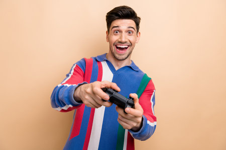 Portrait of cheerful overjoyed person hold controller enjoy play video games isolated on beige color...
