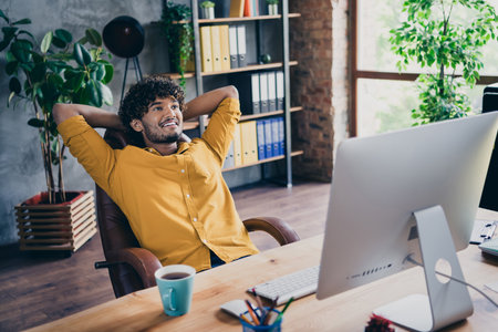 Photo portrait of attractive young man wear yellow shirt hands behind head dream successful startup work modern workplace room home designの写真素材