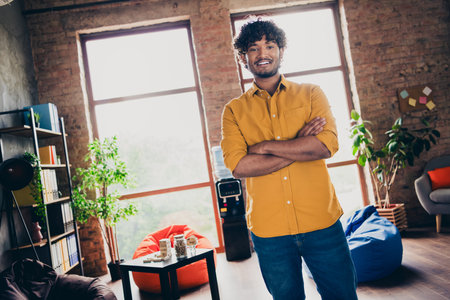 Photo portrait of young male wear yellow shirt crossed hands confident pose work sit table interior loft industrial styleの写真素材