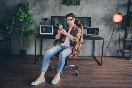 Full body portrait of serious successful agent guy sit chair use smart phone typing email workplace...