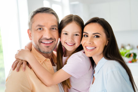 Photo of good mood toothy husband wife little girl smiling embracing together indoors apartment...