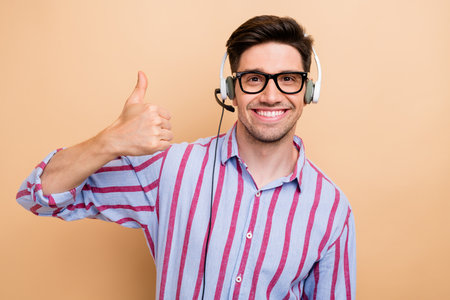Photo of young customer care support manager man wearing headset with microphone thumb up like his job isolated on beige color backgroundの写真素材